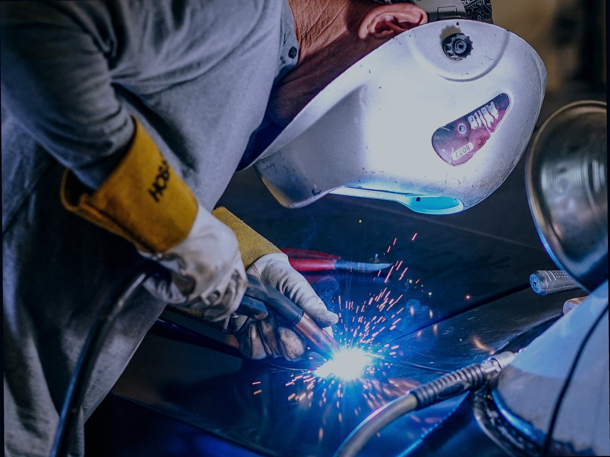 Welder in a helmet MIG welding a car body panel